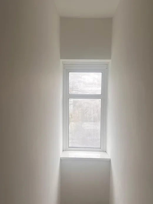 The same stairwell after renovation, replastered and decorated in white with natural light from the landing window